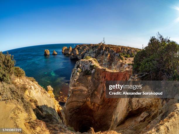 blue water and yellow huge rocks on the ocean shore. portugal. - klippe fotografías e imágenes de stock