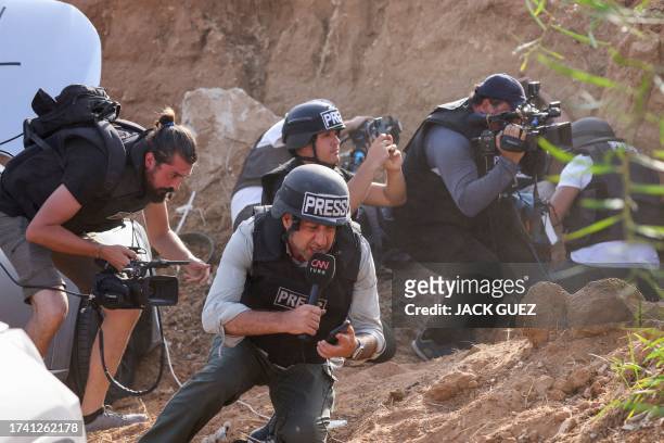 Reporters take cover upon hearing sirens warning of an incoming rocket attack from Gaza, in the southern Israeli city of Sderot, on October 23 amid...