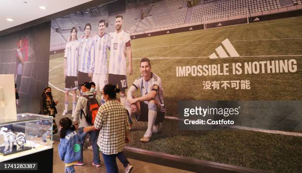 Customers pass an Adidas advertisement featuring Lionel Messi at the Adidas flagship store in Shanghai, China, October 22, 2023.