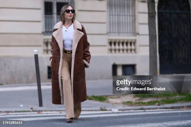 Emy Venturini wears sunglasses, a white tank top from Zara, vintage beige pants, a Hermes belt, a long brown aviator coat with sheep wool inner...