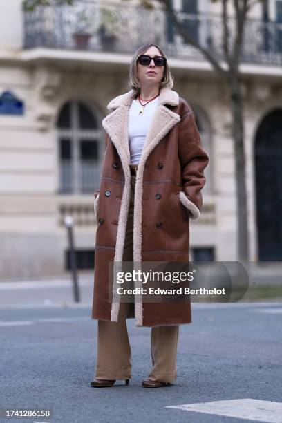 Emy Venturini wears sunglasses, a white tank top from Zara, vintage beige pants, a Hermes belt, a long brown aviator coat with sheep wool inner...