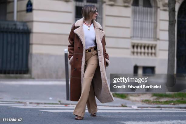 Emy Venturini wears sunglasses, a white tank top from Zara, vintage beige pants, a Hermes belt, a long brown aviator coat with sheep wool inner...