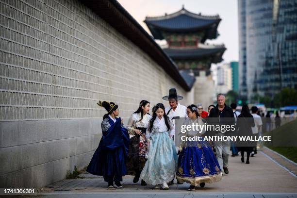 People wearing traditional Hanbok dresses walk along a street outside the Gyeongbokgung Palace in Seoul on October 23, 2023. A woldae terrace for...