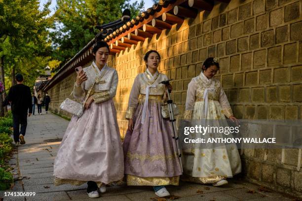 Women wearing traditional Hanbok dresses walk along a street outside the Gyeongbokgung Palace in Seoul on October 23, 2023. A woldae terrace for...
