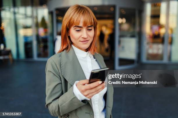 geschäftsfrau, die vor dem gebäude sms schreibt - business woman stock-fotos und bilder