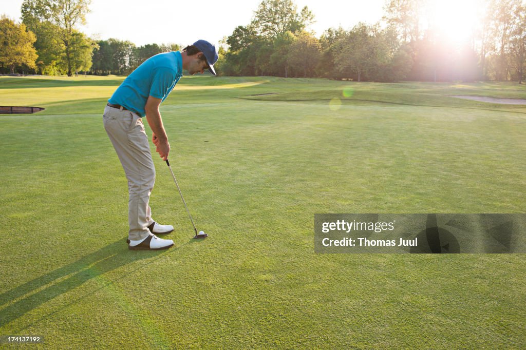 Male golfer putting at sunrise