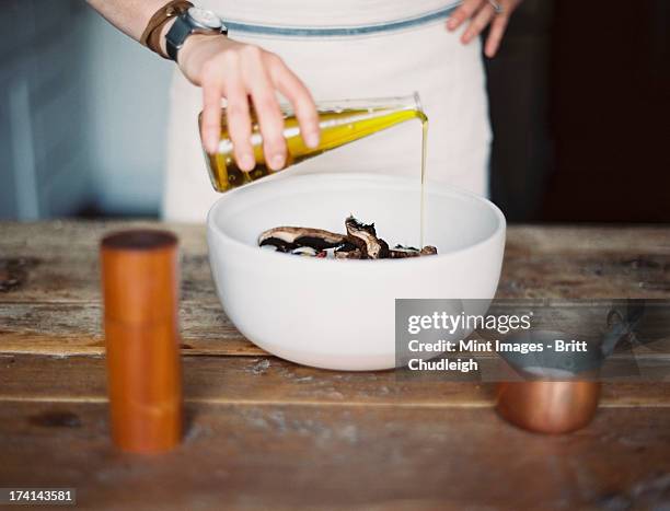 a domestic kitchen. a woman wearing an apron, dressing a fresh salad of vegetables in a bowl with oil.  - food dressing stock pictures, royalty-free photos & images