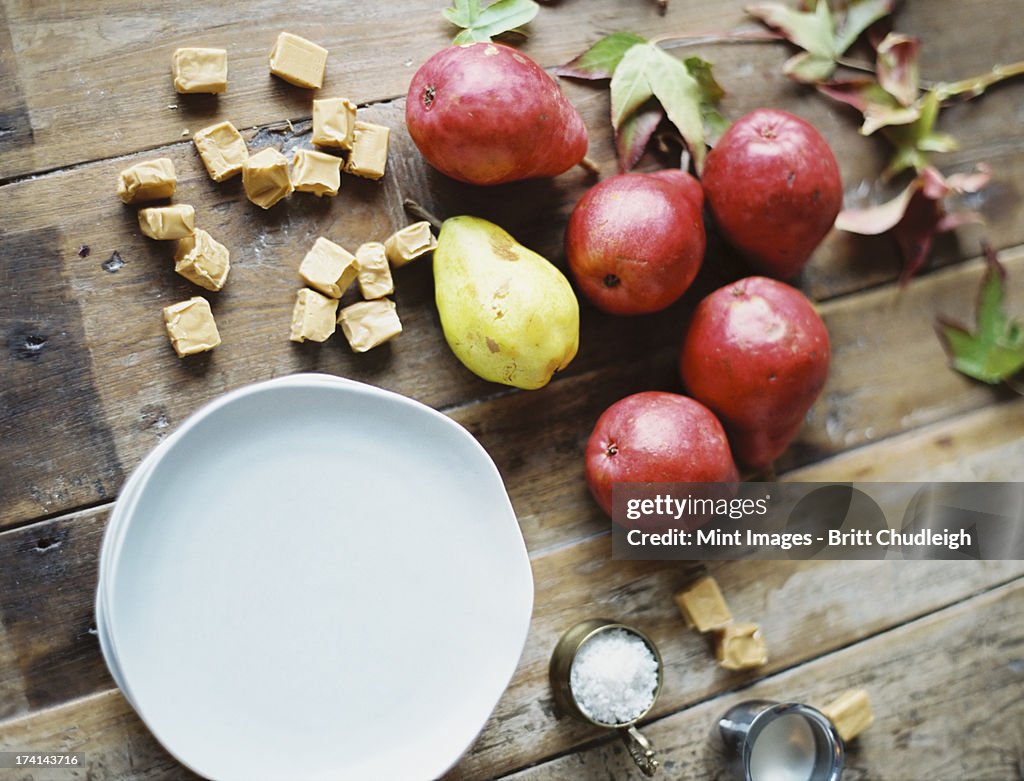 A domestic kitchen tabletop. A small group of fresh organic pears and a stack of white plates.