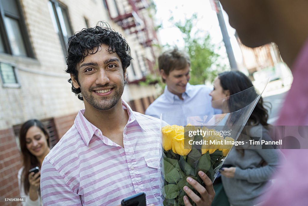 Urban Lifestyle. New York city street. A group of five people, one man carrying a bunch of flowers and a woman checking her phone. 