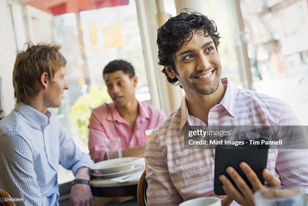 Urban Lifestyle. Three young men around a table in a cafe. One holding a digital tablet.