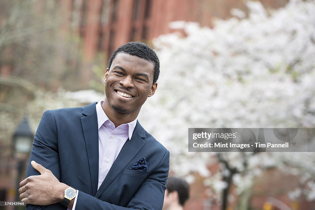 City life in spring. A man in a blue suit with arms folded, in a city park. 