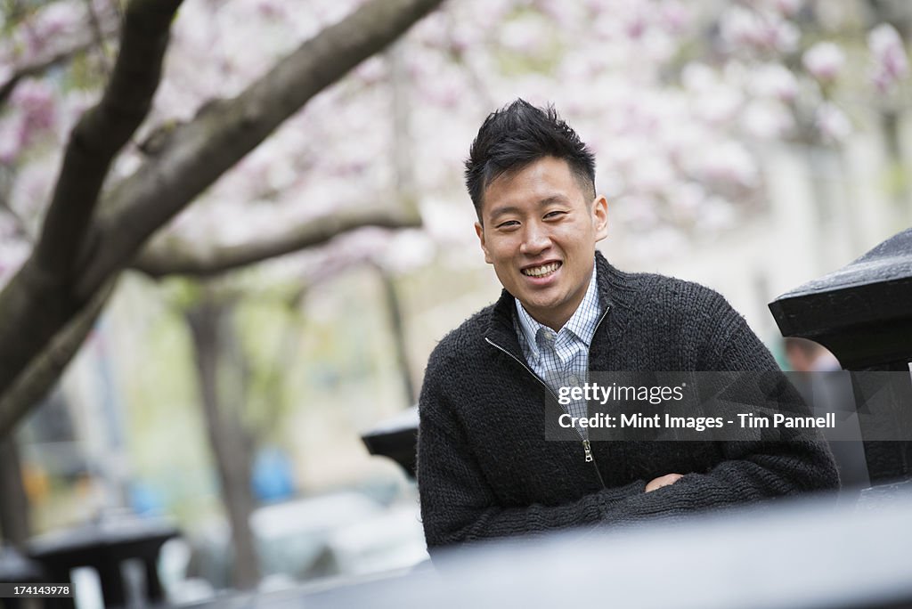 City life in spring. A young man outdoors in a city park. Sitting on a bench.