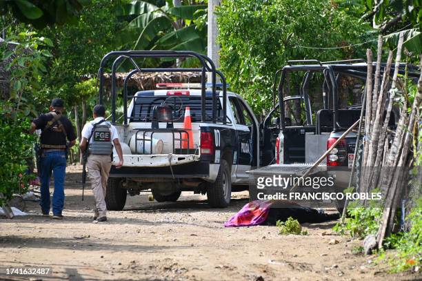 Security forces pass by a corpse as they inspect the area where at least 11 police officers were killed in an ambush by criminal groups in Coyuca de...