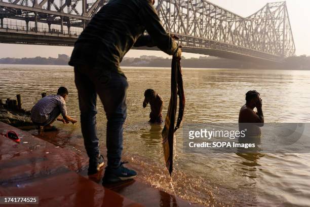 People are seen washing and performing morning pujas at the Hooghly river with the Howrah bridge in the background.