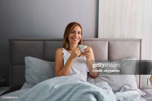 happy woman having her morning coffee in bed. - pyjamas stock pictures, royalty-free photos & images