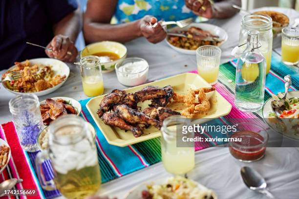 black family enjoying jamaican food outdoors - jerk chicken stockfoto's en -beelden