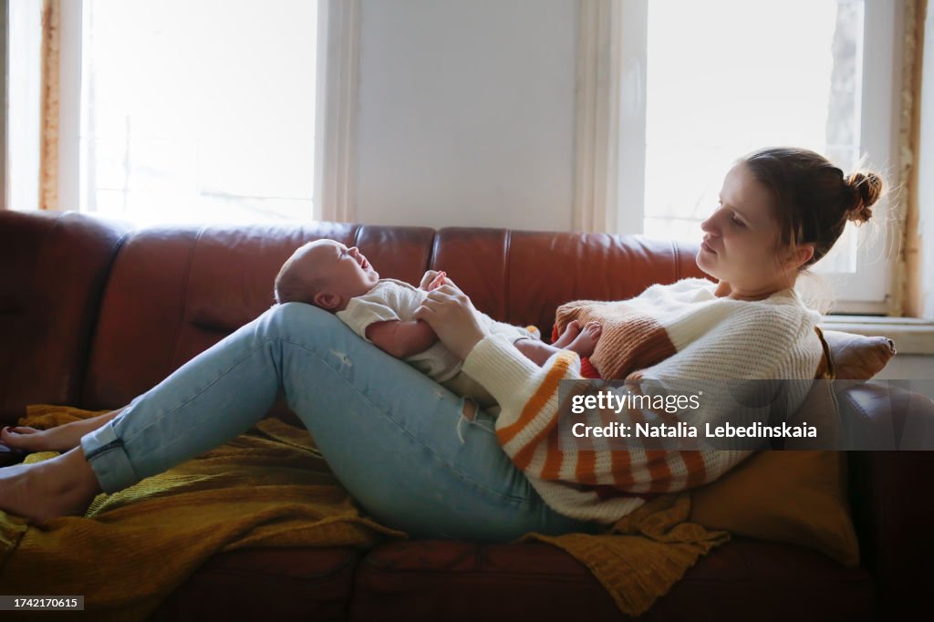 Burnt out tired mother in depression rocks crying baby on her lap