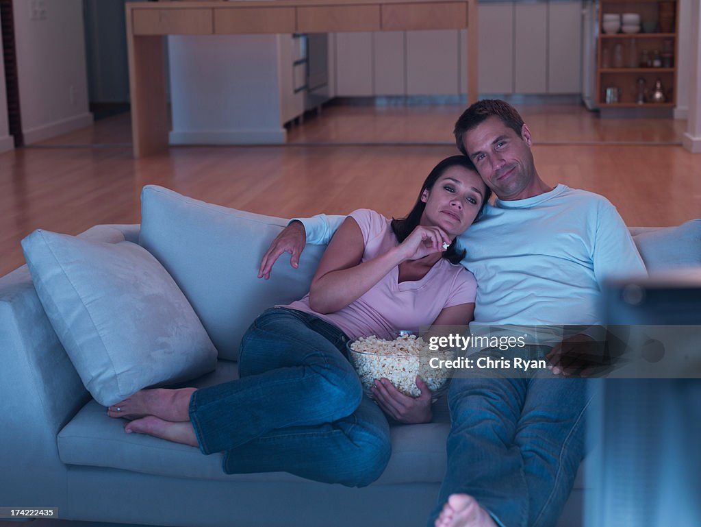 Donna e uomo con popcorn sul divano guardando la televisione