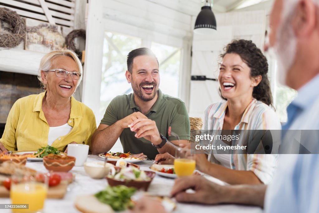 Happy adult offspring talking to their parents during a meal at dining table.