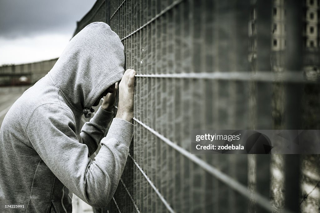 Lonely Man with Hood Leaning on a Fence