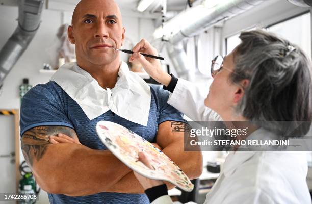 An employee adjusts the skin tone on the wax effigy of Dwayne Johnson, after the US actor complained about its pale skin tone, at the Grevin museum...