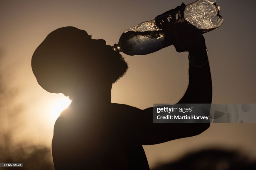 Black African man in silhouette drinking water from a bottle. Climate change, Global warming, heat