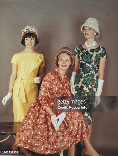 Posed studio portrait of three female fashion models wearing, from left, a short sleeved belted dress in Laburnum yellow silk, a poppy print coral...