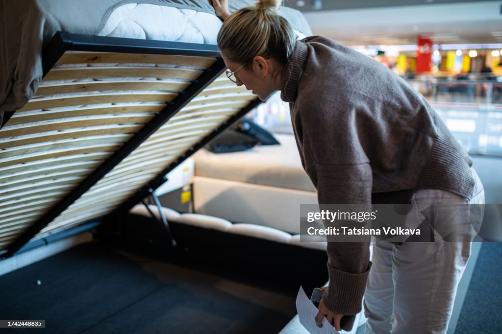 Determined mature lady engages in thorough examination of bed in furniture store