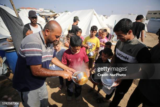 Palestinian children receive food between tents set up for Palestinians seeking refuge on the grounds of a United Nations Relief and Works Agency for...