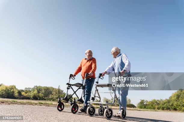 two old friends walking on a country road, using wheeled walkers - looprek stockfoto's en -beelden