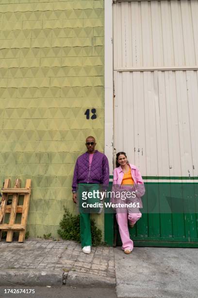 fashionable couple leaning together on wall at footpath - multi colored coat stock pictures, royalty-free photos & images