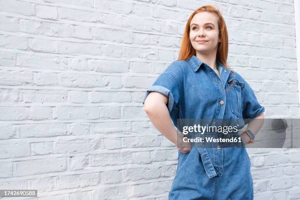 smiling businesswoman standing with arms akimbo near wall - mano sobre la cadera fotografías e imágenes de stock