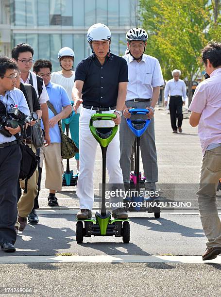The mayor of Japan's Tsukuba City, Kenichi Ichihara , and Toyota Motor partner robot director Akifumi Tamaoki ride on Toyota's transport assistance...
