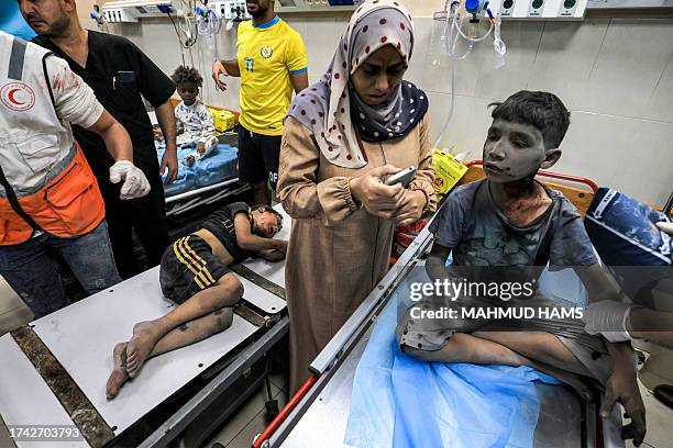 Graphic content / A woman uses a phone while waiting with two children injured in Israeli bombardment about to receive emergency treatment at a...