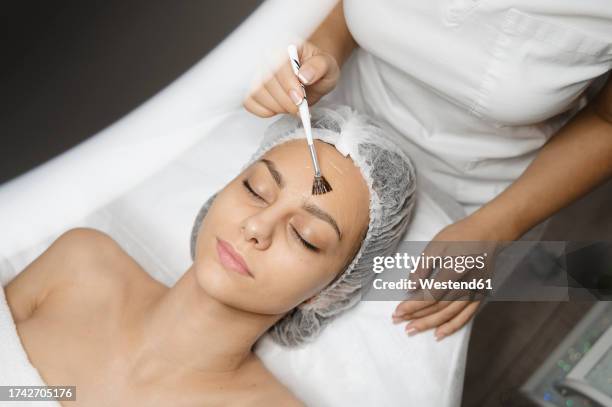 dermatologist applying chemical peel with brush on woman's face - esteticista fotografías e imágenes de stock