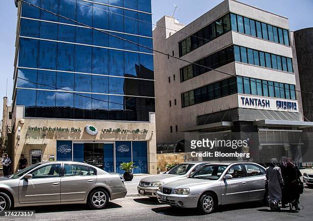 Pedestrians pass automobiles parked outside a branch of Jordan Dubai Islamic Bank in the financial district in Amman, Jordan, on Sunday, July 21,...