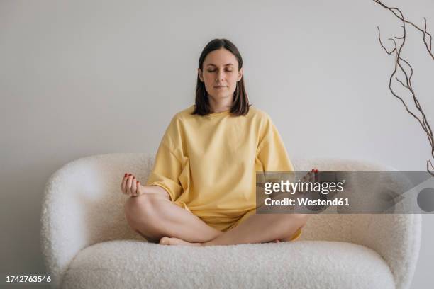 woman meditating on sofa at home - mudra stock-fotos und bilder