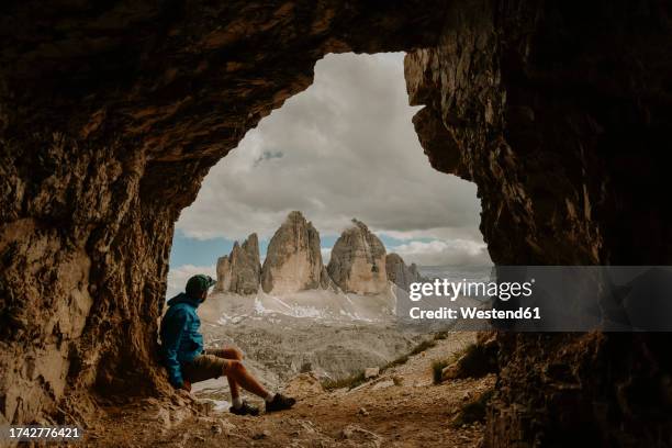 italy, male hiker looking at three peaks of lavaredo from cave entrance - naturpark stock-fotos und bilder
