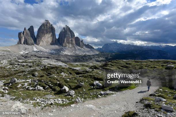 italy, female hiker following road toward three peaks of lavaredo - austrian alps stock pictures, royalty-free photos & images