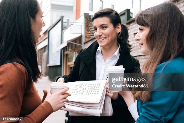 smiling businesswoman holding newspaper and talking to office colleagues - long coat stock pictures, royalty-free photos & images