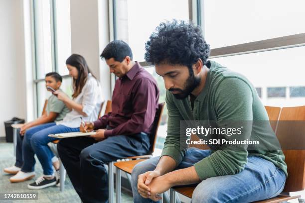 in waiting room, young adult man does serious thinking - sala de espera imagens e fotografias de stock