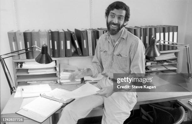 View of American journalist and author Jamie Kalven as he smiles, perched on the edge of a desk in an office at the University of Chicago, Chicago,...