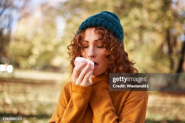 redhead woman sneezing at autumn park - cold virus stock pictures, royalty-free photos & images