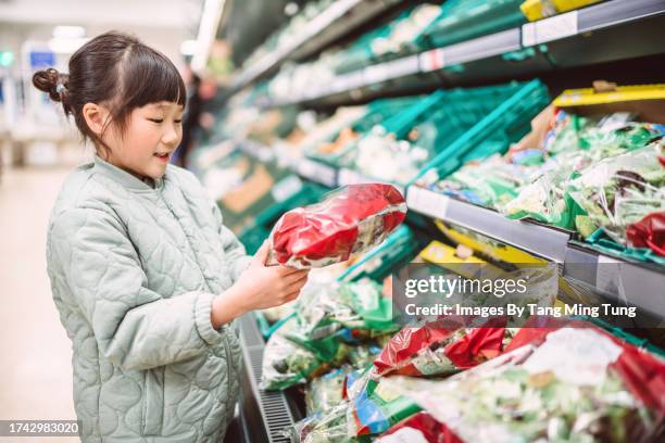 lovely cheerful girl choosing packaged vegetable from the refrigerator while doing groceries shopping with family in supermarket - child food stock pictures, royalty-free photos & images