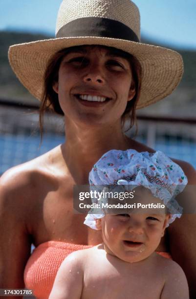 Princess Caroline of Monaco, wearing a swimming costume and straw hat, together with her second child Charlotte, who is wearing a flowery hat. 1987..