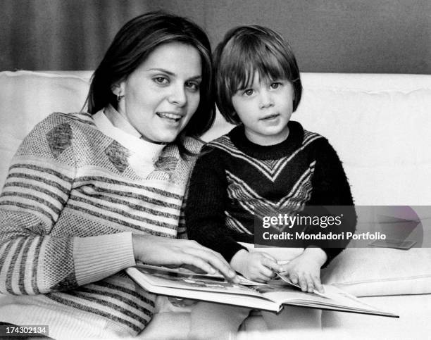 Italian actress Silvia Dionisio reading a book on the sofa with her son and Italian actor Saverio Deodato Dionisio. Rome, 1970s.