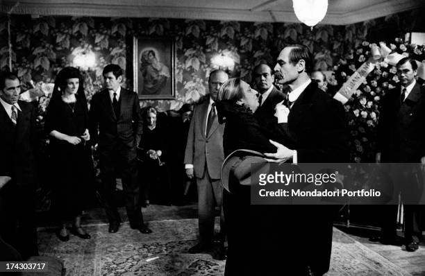 Scene of the movie The Valachi Papers: Joseph Wiseman supports Pupella Maggio during the funeral of Reina, a Mafia leader, surrounded by other people...