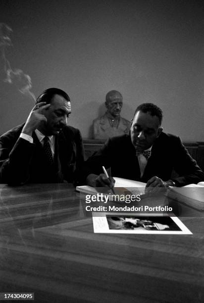 American writer Richard Wright sitting at a desk and writing beside Italian publisher, journalist and writer Alberto Mondadori during a press...