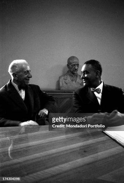 American writer Richard Wright sitting at a desk and smiling at a man during a press conference. Richard Wright is visiting Italy for the publication...