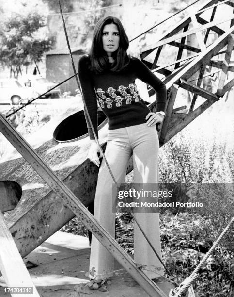 Italian actress Laura Belli posing leaning on a metal structure. Rome, 1975.